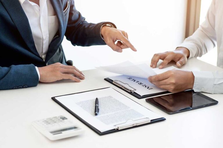 A person reviews an insurance bill and calendar while holding a payment envelope at their kitchen table.